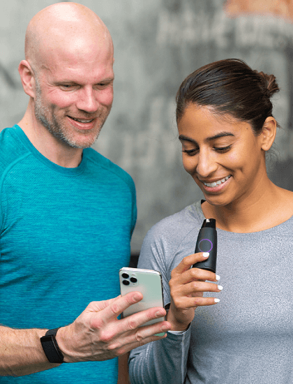 2 smiling people one holding a phone and the other holding a Lumen device