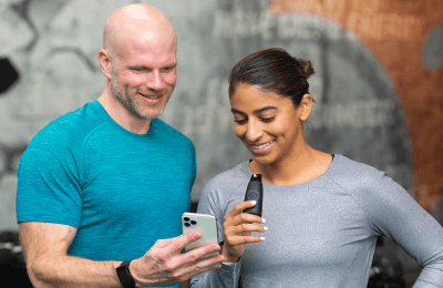 A man and a woman are smiling, the man is holding a cell phone and the woman is holding a Lumen device